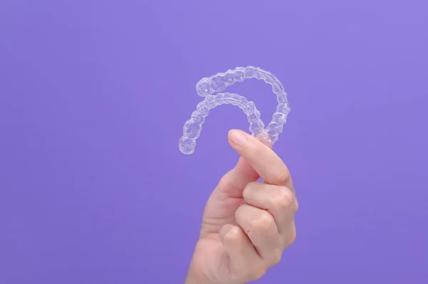 close up of woman's hand holding invisalign braces in studio, dental healthcare and Orthodontic concept.	