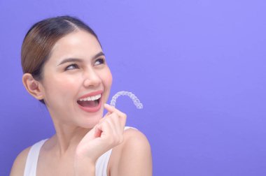 A young smiling woman holding invisalign braces in studio, dental healthcare and Orthodontic concept.	