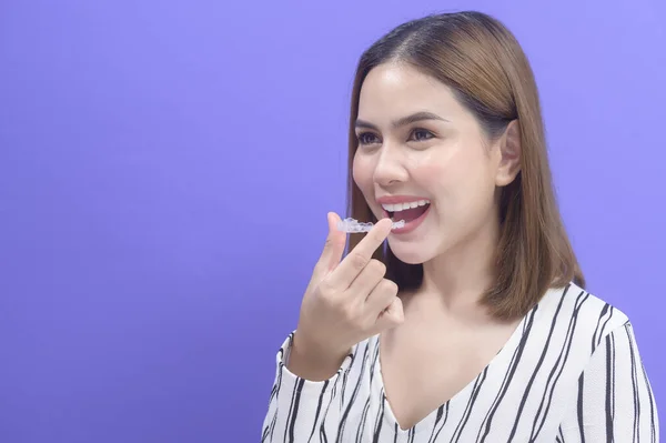 A young smiling woman holding invisalign braces in studio, dental healthcare and Orthodontic concept.	