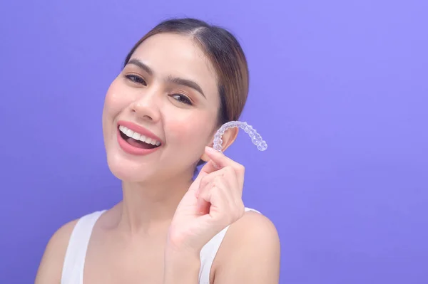 A young smiling woman holding invisalign braces in studio, dental healthcare and Orthodontic concept.	