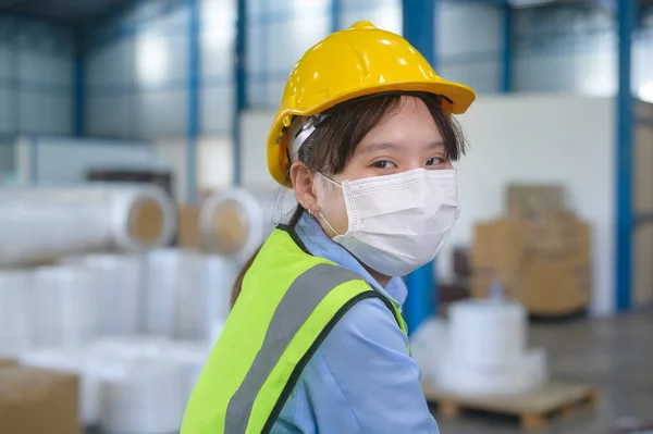 An engineering woman wearing medical mask , protective helmet working in warehouse factory