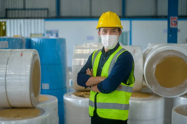 An engineering man wearing medical mask , protective helmet working in warehouse factory