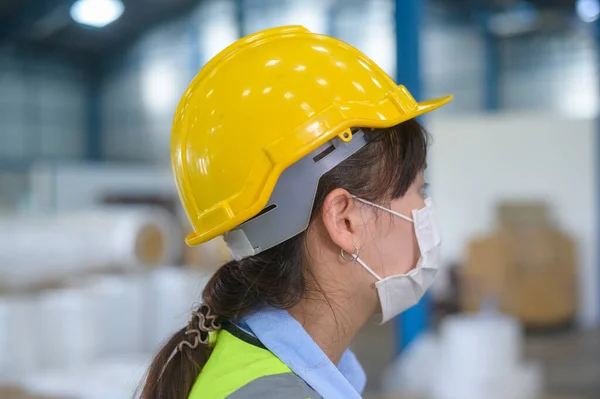 An engineering woman wearing medical mask , protective helmet working in warehouse factory