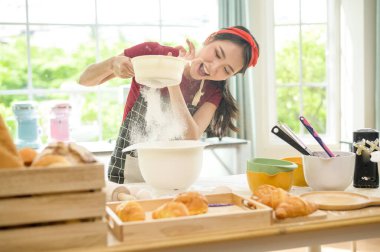 Genç ve güzel bir Asyalı kadın mutfağında, fırınında ve kahve dükkanında yemek pişiriyor. 