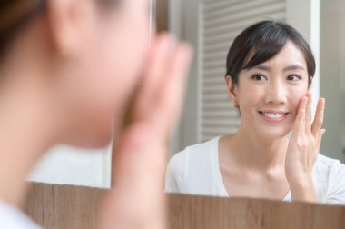 Mutlu güzel bir kadın yüzüne nemlendirici krem sürüyor, cilt bakımı ve tedavi konsepti.