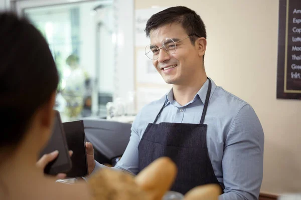 Smiling barista giving online payment to  customer , pay for the order in a cafe shop