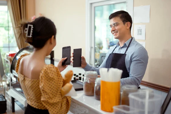 Smiling barista giving online payment to  customer , pay for the order in a cafe shop