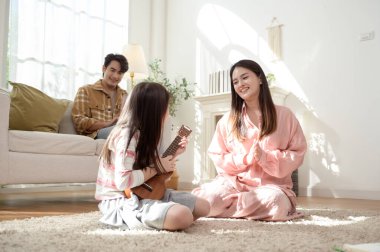 Anne ve babası oturma odasında keyfine bakarken kız ukulele çalıyor..