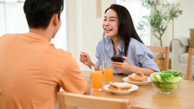 Çift kahvaltıyla bir masaya oturur. Biri dizüstü bilgisayarda çalışırken diğeri telefon kullanıyor..