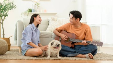 Çift evde köpekleriyle birlikte yerde oturuyor. Biri dinlenirken gitar çalar..