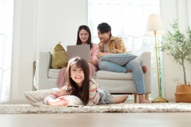 Ailesi kanepede oturup dizüstü bilgisayarla çalışırken kız yerde resim çiziyor..