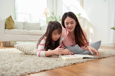 Bir kız ve annesi evde dinlenirken yerde birlikte kitap okuyorlar..