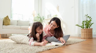 Bir kız ve annesi evde dinlenirken yerde birlikte kitap okuyorlar..