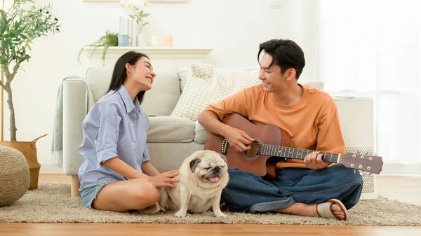 Çift evde köpekleriyle birlikte yerde oturuyor. Biri dinlenirken gitar çalar..