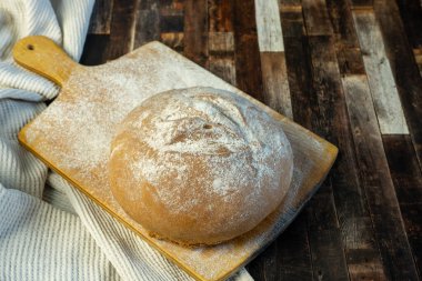 İştah açıcı taze pişmiş ekmek az önce masaya kondu. Görüntü ayrıca un kaplı kesme tahtası ve kumaştan oluşan kahverengi bir arkaplan içerir. Ev yapımı ekmek, fırın..