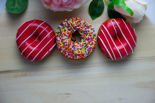 Tre Ciambelle Diversi Colori Trovano Uno Stand Legno Accanto Una — Foto Stock