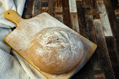 İştah açıcı taze pişmiş ekmek az önce masaya kondu. Görüntü ayrıca un kaplı kesme tahtası ve kumaştan oluşan kahverengi bir arkaplan içerir. Ev yapımı ekmek, fırın..