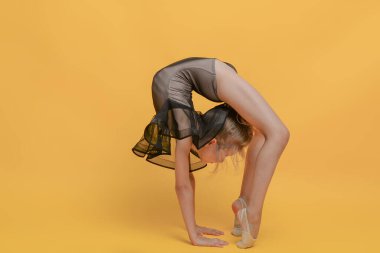 Küçük esnek kız jimnastikçi farklı egzersizler yapıyor ve sarı arka planda poz veriyor.