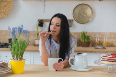 Genç, güzel, modern bir kadın mutfaktaki masanın yanında duruyor..