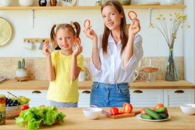Anne ve küçük kızı mutfakta sağlıklı yiyecekler hazırlayıp çay içiyorlar.