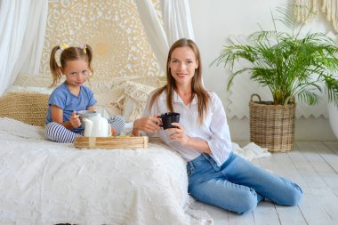 Mutlu anne ve küçük kız birlikte sıcak çay içip evde kahvaltı ediyorlar.