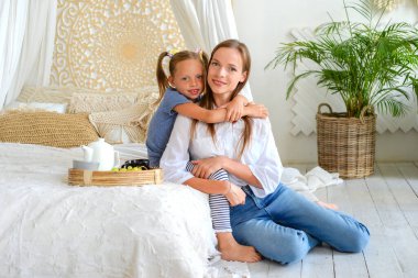 Mutlu anne ve küçük kız birlikte sıcak çay içip evde kahvaltı ediyorlar.