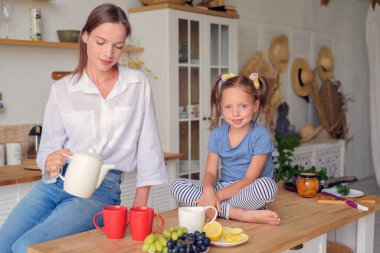Anne ve küçük kızı mutfakta çay içip birlikte kahvaltı ediyorlar. aile portresi