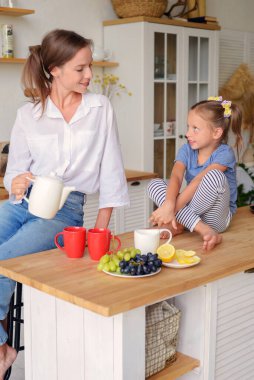 Anne ve küçük kızı mutfakta çay içip birlikte kahvaltı ediyorlar. aile portresi