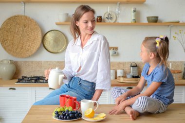 Anne ve küçük kızı mutfakta çay içip birlikte kahvaltı ediyorlar. aile portresi