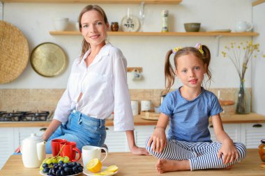 Anne ve küçük kızı mutfakta çay içip birlikte kahvaltı ediyorlar. aile portresi