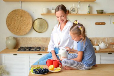 Anne ve küçük kızı mutfakta çay içip birlikte kahvaltı ediyorlar. aile portresi