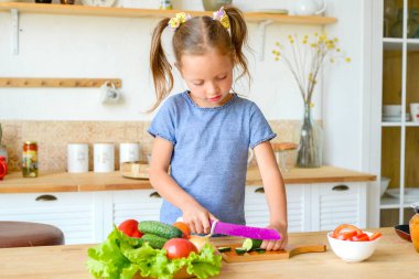 Mutfaktaki küçük kız salata için sebze kesiyor. Doğru beslenme ve vejetaryenlik kavramı