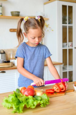 Mutfaktaki küçük kız salata için sebze kesiyor. Doğru beslenme ve vejetaryenlik kavramı