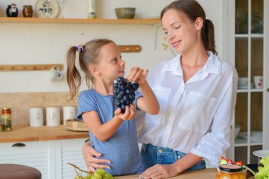 Annesiyle birlikte mutfakta üzüm yiyen tatlı bir kız.