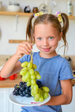 Mutfaktaki küçük tatlı kız. Sağlıklı yiyecekler hazırlar ve yer.