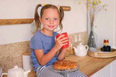 Mutfaktaki küçük kız limonlu çay içiyor.