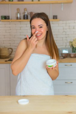 Bir kadın yüzündeki güzel teniyle ilgilenir. Genç bir kadın yüzüne nemlendirici sürüyor. Gülümseyen kız elinde bir kavanoz krem tutarak losyon sürüyor..