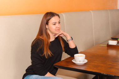 Güzel genç bir kadın, rahat bir kafede kahve içiyor.