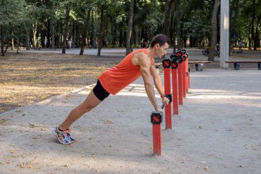 Atletik güçlü adam parkta sokak makineleri ve yatay barlarla antrenman yapıyor.