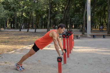 Atletik güçlü adam parkta sokak makineleri ve yatay barlarla antrenman yapıyor.