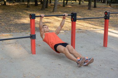 Atletik güçlü adam parkta sokak makineleri ve yatay barlarla antrenman yapıyor.