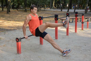 Atletik güçlü adam parkta sokak makineleri ve yatay barlarla antrenman yapıyor.