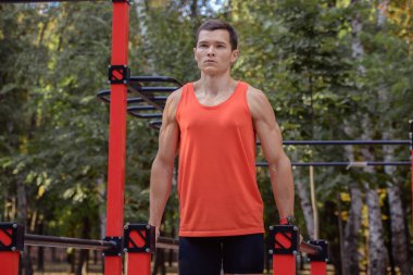 Atletik güçlü adam parkta sokak makineleri ve yatay barlarla antrenman yapıyor.