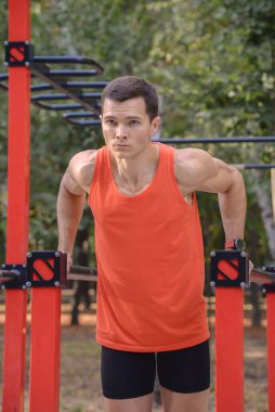 Atletik güçlü adam parkta sokak makineleri ve yatay barlarla antrenman yapıyor.