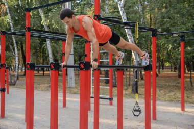 Atletik güçlü adam parkta sokak makineleri ve yatay barlarla antrenman yapıyor.