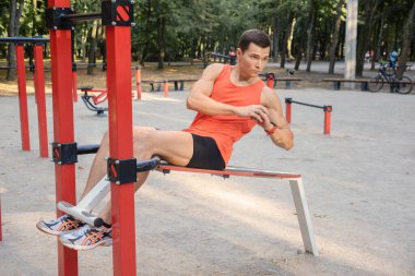 Atletik güçlü adam parkta sokak makineleri ve yatay barlarla antrenman yapıyor.