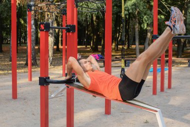 Atletik güçlü adam parkta sokak makineleri ve yatay barlarla antrenman yapıyor.