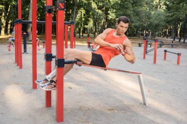 Atletik güçlü adam parkta sokak makineleri ve yatay barlarla antrenman yapıyor.