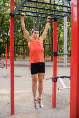Atletik güçlü adam parkta sokak makineleri ve yatay barlarla antrenman yapıyor.