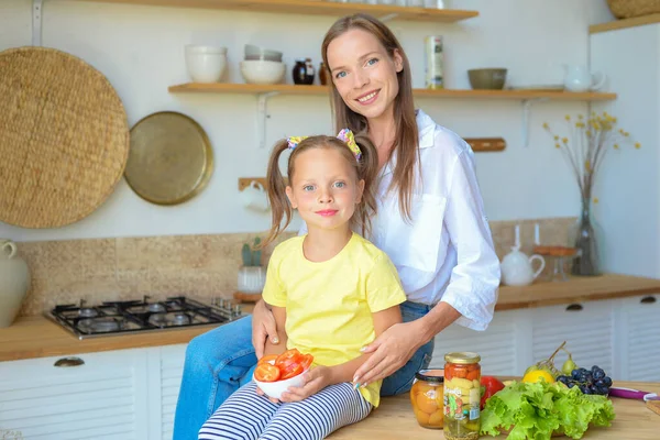 Anne ve küçük kızı mutfakta sağlıklı yiyecekler hazırlayıp çay içiyorlar.